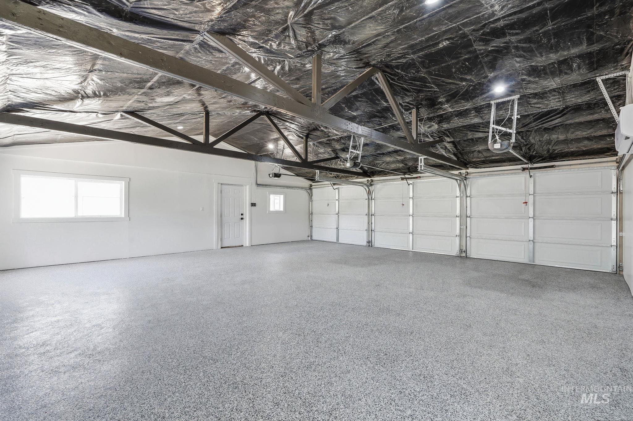 2152 Artesian Road Eagle, ID 83616 - Photo 33 of 50 Spacious garage featuring a speckled epoxy floor, four garage doors, exposed ceiling trusses, and multiple windows providing natural light