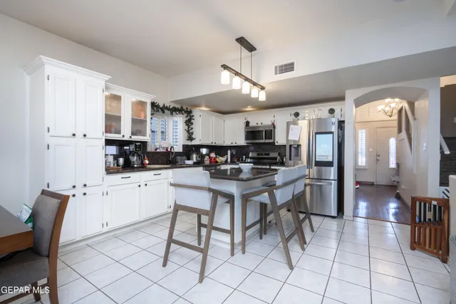 a kitchen with stainless steel appliances kitchen island granite countertop a stove a refrigerator a sink a dining table and chairs with white cabinets