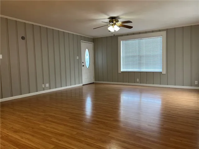 an empty room with wooden floor chandelier fan and windows
