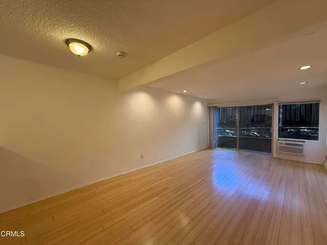 an empty room with wooden floor and kitchen view