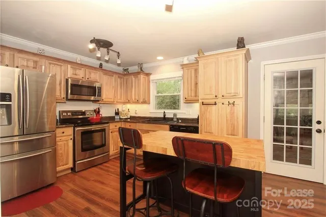 a kitchen with stainless steel appliances granite countertop a stove top oven a refrigerator a dining table and chairs with wooden floor