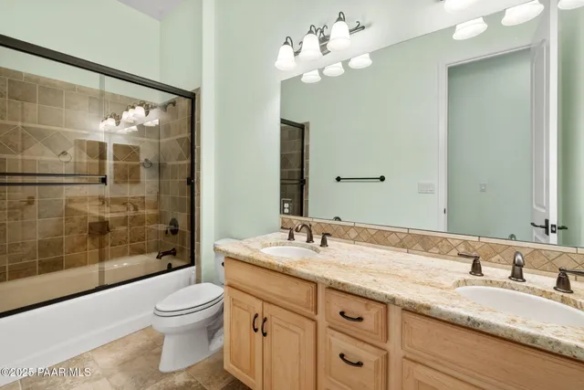 a bathroom with a granite countertop double vanity sink a mirror and a shower