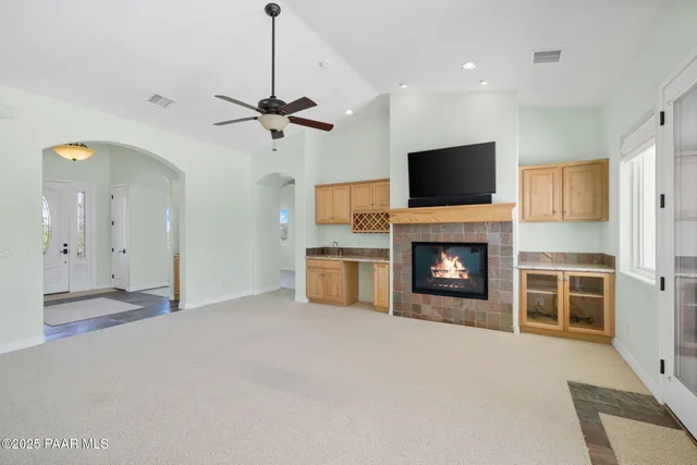 a view of a livingroom with a fireplace a ceiling fan and a kitchen view