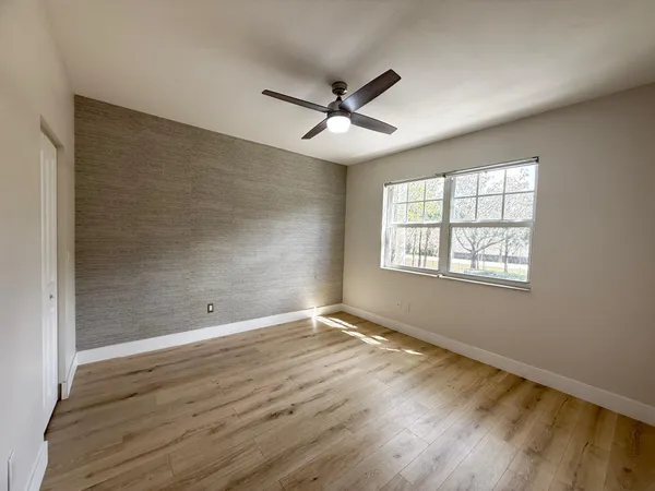 an empty room with wooden floor ceiling fan and windows