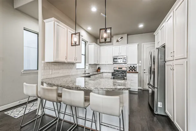 a kitchen with granite countertop a refrigerator a stove a sink and white cabinets with wooden floor