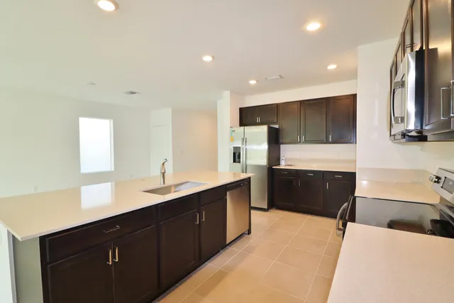 a large kitchen with stainless steel appliances a sink dishwasher a stove and black cabinets with wooden floor