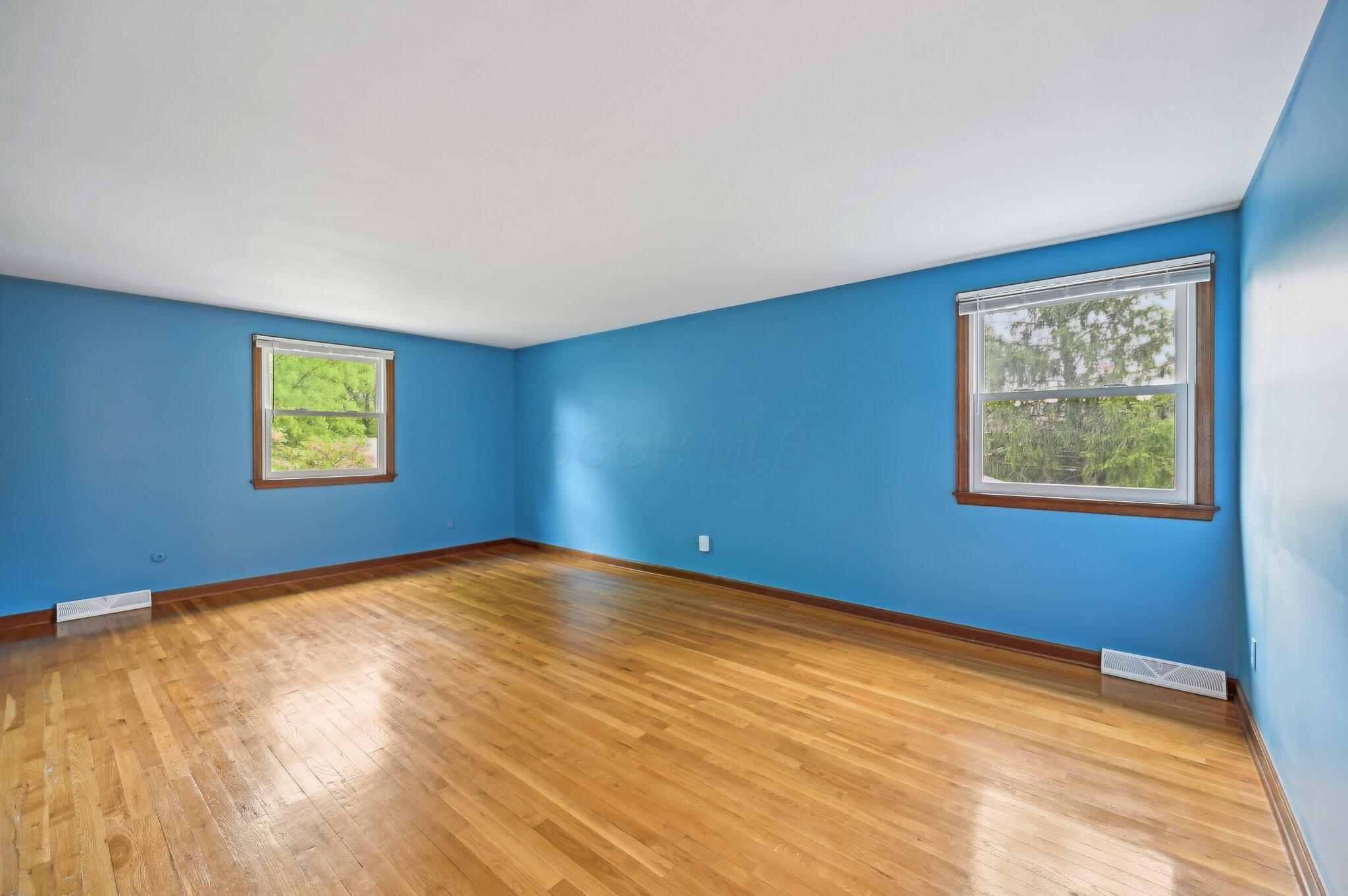 5917 Rocky Rill Road Columbus, OH 43235 - Photo 22 of 47 Spacious primary bedroom with hardwood floors, two large windows, and fresh blue paint throughout.