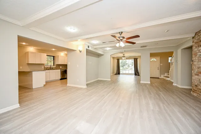 a view of an empty room and kitchen view with wooden floor