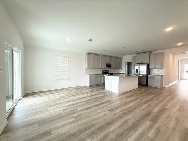 a view of an empty room with window and a kitchen