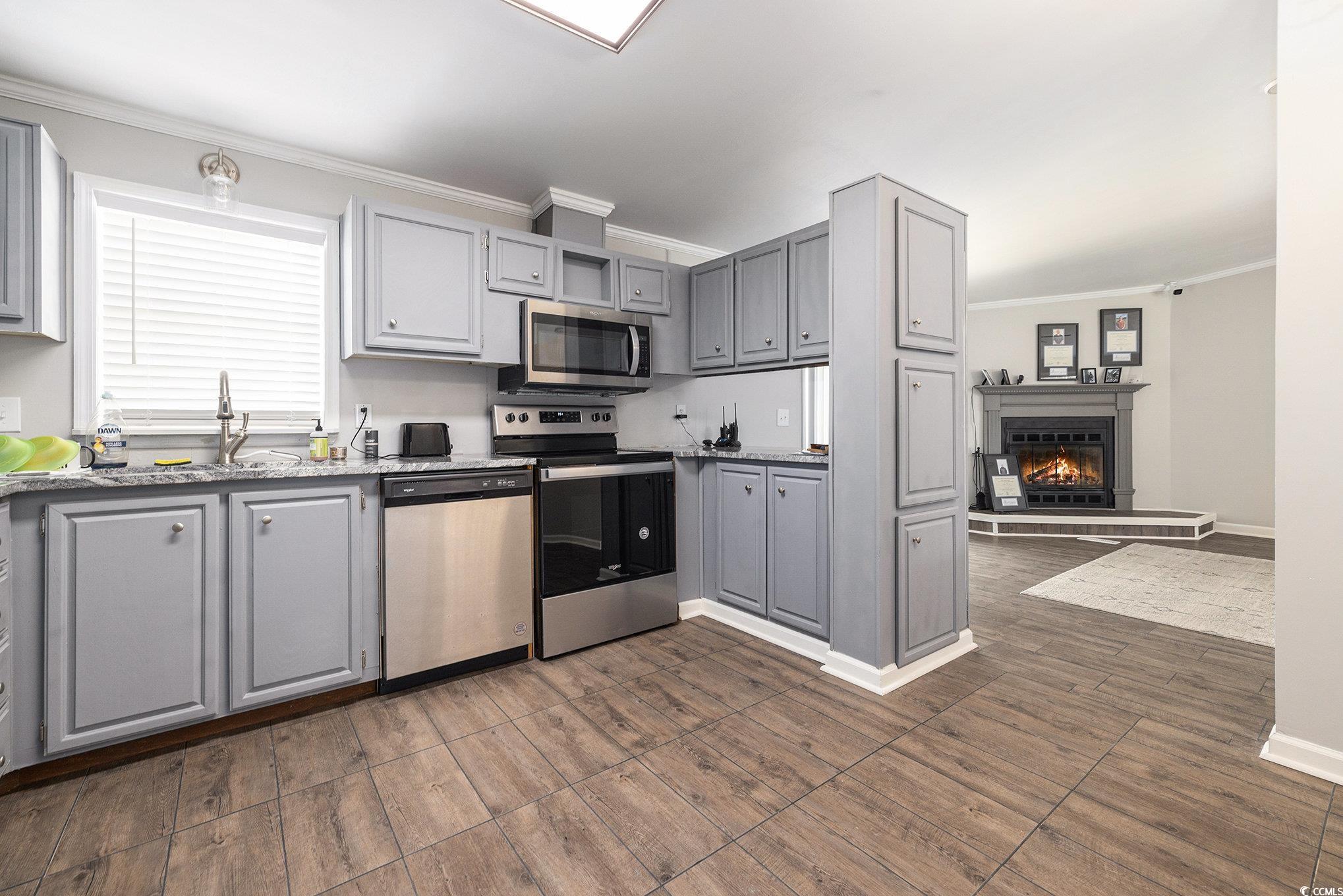 3843 Kelly Road Conway, SC 29526 - Photo 14 of 40 Kitchen featuring appliances with stainless steel finishes, gray cabinets, crown molding, dark wood finished floors, and a fireplace