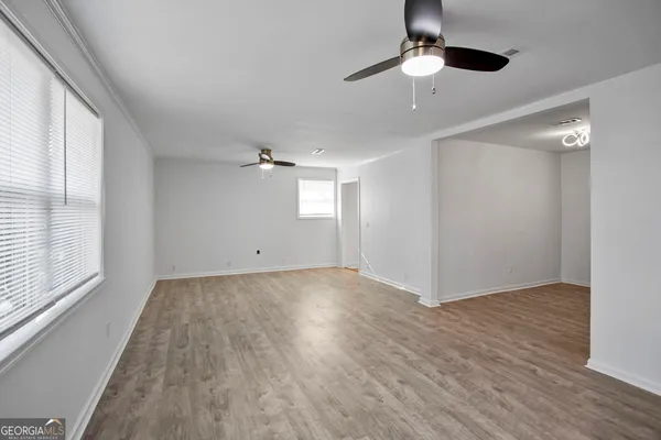 an empty room with wooden floor chandelier fan and windows