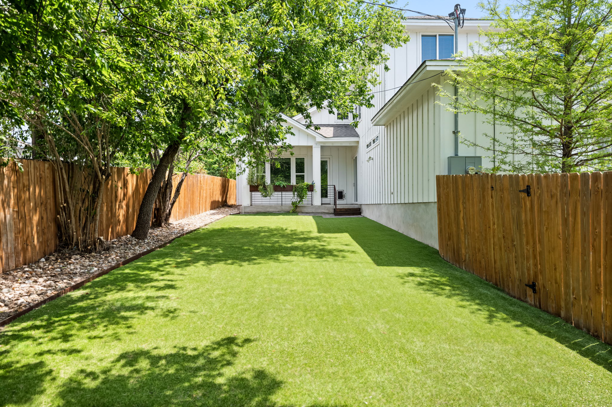 1902 Webberville Road, Unit B Austin, TX 78721 - Photo 31 of 39 A pristine lawn stretches towards a contemporary white-sided residence, framed by a sturdy wooden fence.