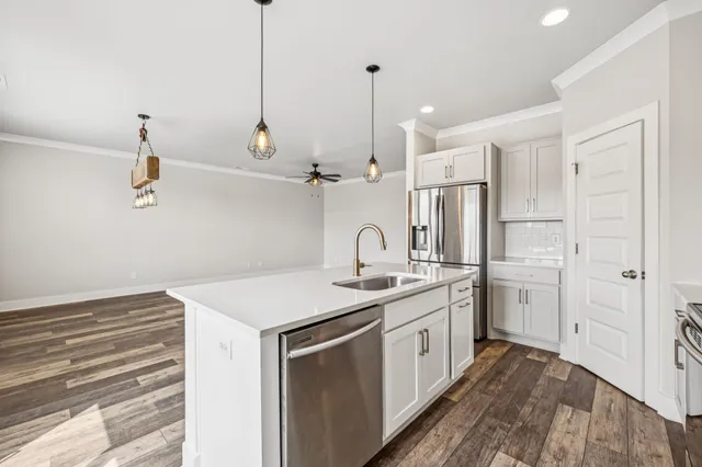 a kitchen with a sink dishwasher a refrigerator and white cabinets with wooden floor