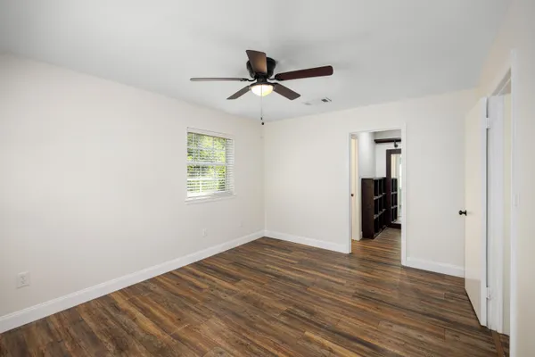 an empty room with wooden floor a ceiling fan & windows