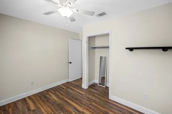 a view of an empty room with wooden floor and a ceiling fan