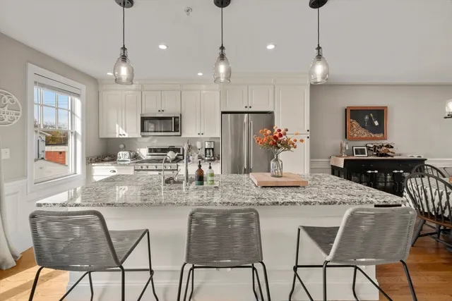 a kitchen with stainless steel appliances granite countertop a dining table chairs refrigerator and cabinets