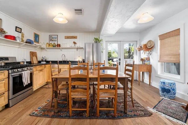 a dining hall with stainless steel appliances kitchen island granite countertop a stove a dining table and chairs with wooden floor