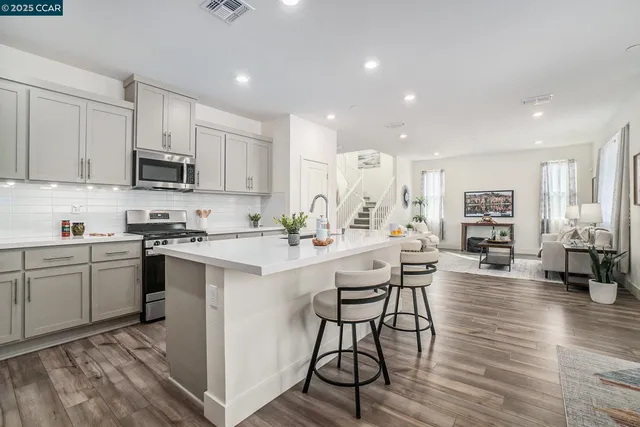 a kitchen with stainless steel appliances kitchen island granite countertop a stove a sink a refrigerator and white cabinets with wooden floor