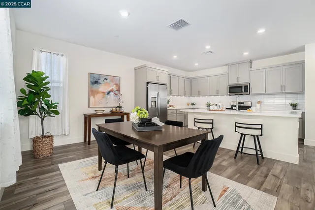 a kitchen with stainless steel appliances kitchen island granite countertop a dining table chairs and white cabinets