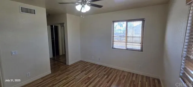 an empty room with wooden floor chandelier fan and windows