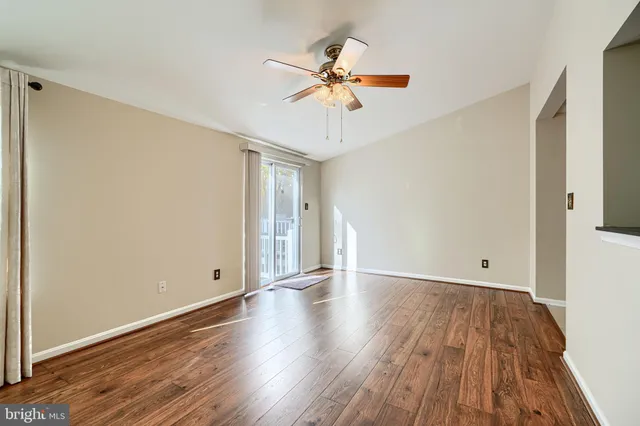 a view of an empty room with wooden floor and a ceiling fan