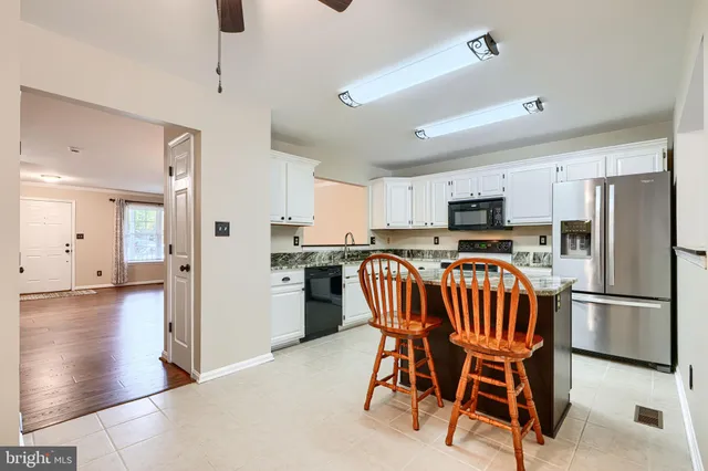 a kitchen with stainless steel appliances kitchen island granite countertop a refrigerator a stove a sink dishwasher and white cabinets with wooden floor