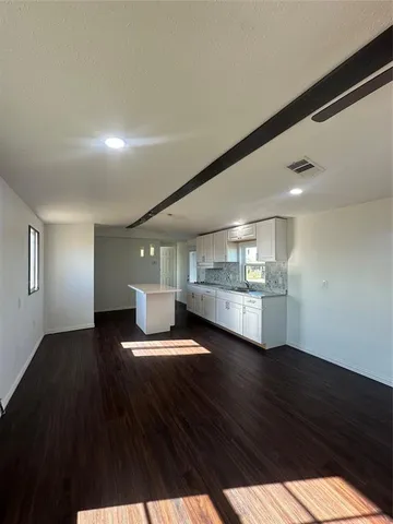 a view of an empty room with wooden floor and a kitchen