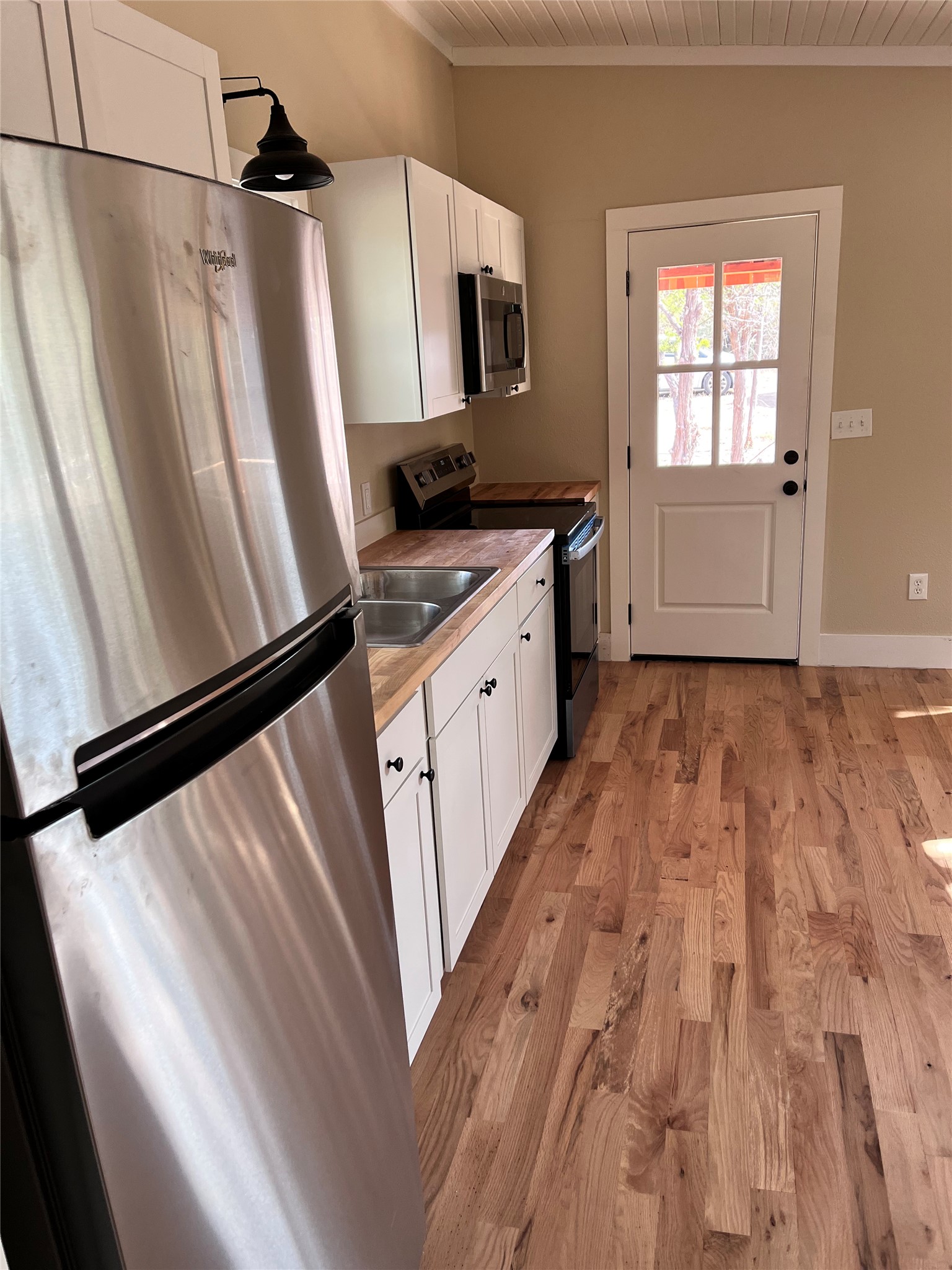 1565 Pump Station Road, Unit B Wimberley, TX 78676 - Photo 5 of 12 Kitchen with white cabinetry, stainless steel appliances, light wood-style flooring, crown molding, and light countertops