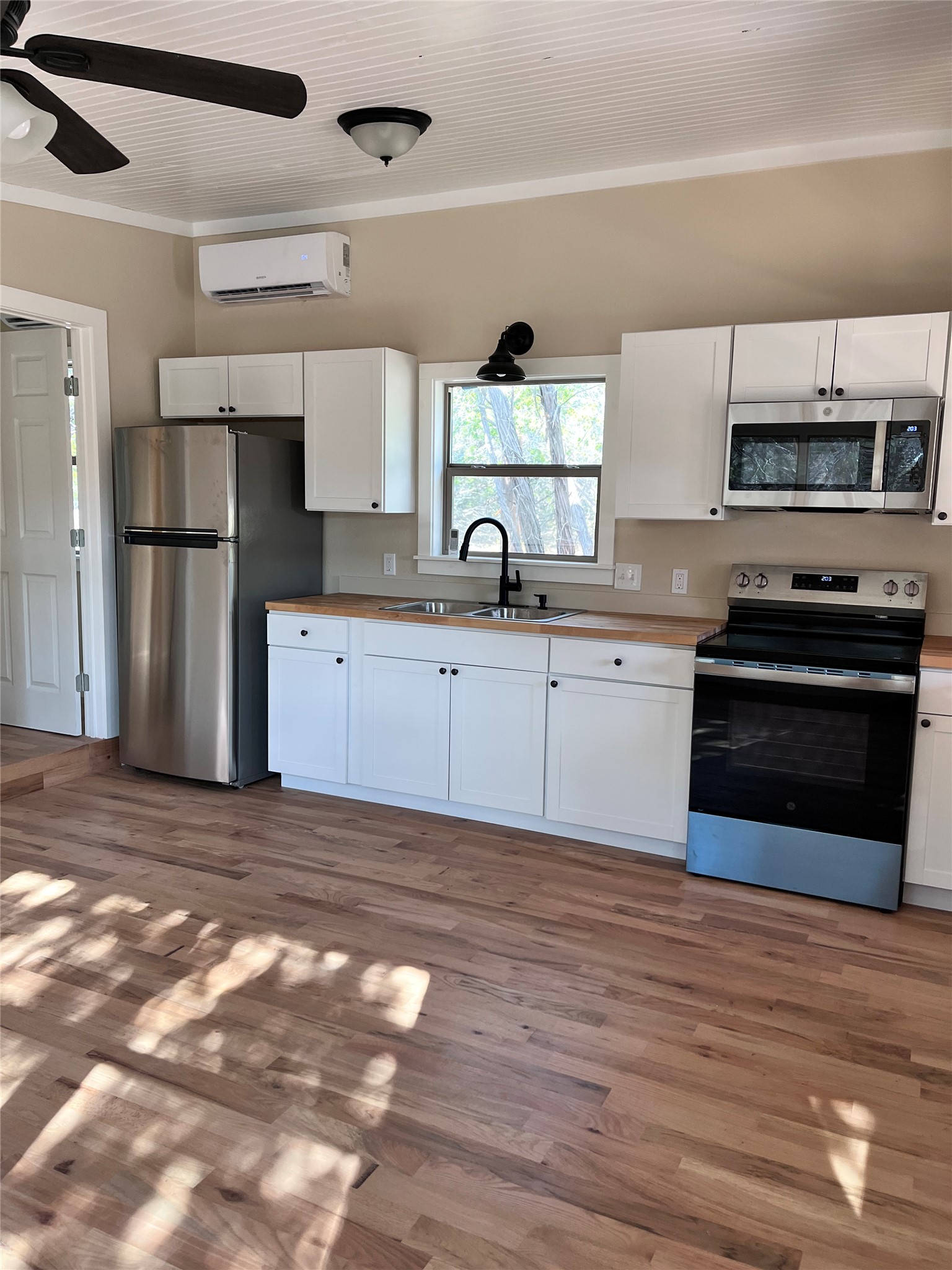 1565 Pump Station Road, Unit B Wimberley, TX 78676 - Photo 6 of 12 Kitchen with white cabinets, stainless steel appliances, a ceiling fan, crown molding, and dark wood-type flooring