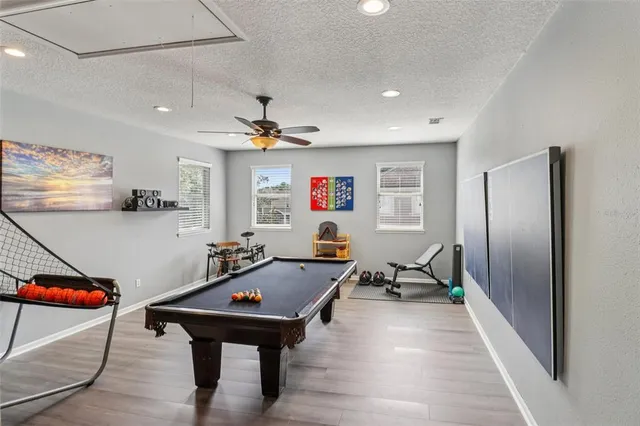 a room with wooden floor pool table furniture and a ceiling fan