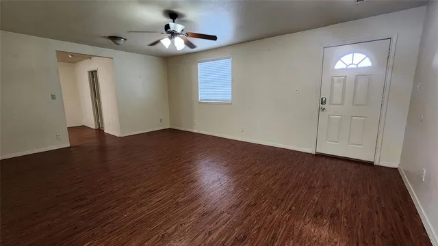 a view of an empty room with wooden floor and a ceiling fan