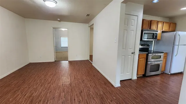a view of kitchen and empty room with wooden floor