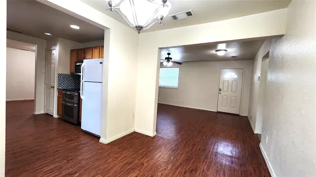a view of an empty room with wooden floor and a kitchen