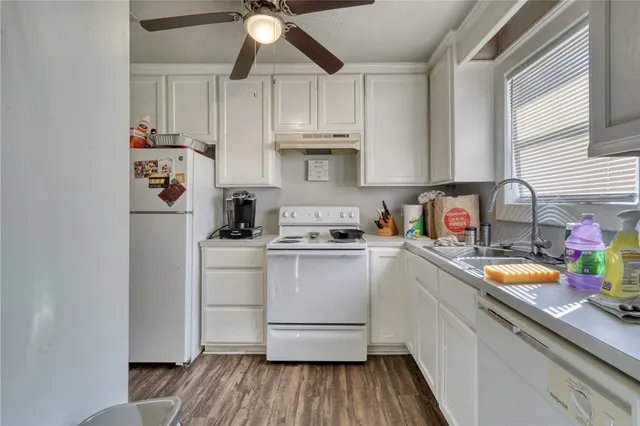 a kitchen with stainless steel appliances granite countertop a sink dishwasher a refrigerator and white cabinets with wooden floor