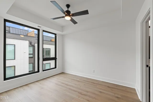 an empty room with wooden floor fan and windows