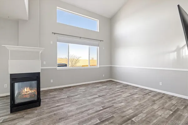 a view of an empty room with wooden floor fireplace and a window