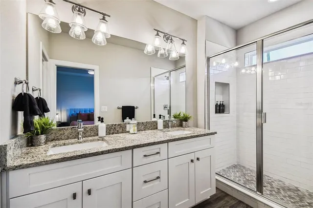 a bathroom with a granite countertop double vanity sink mirror and shower