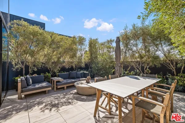 a view of a patio with couches and table and chairs with potted plants and large trees