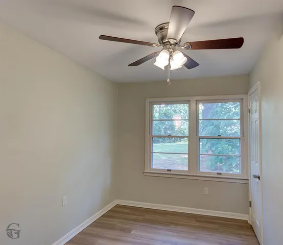 an empty room with wooden floor fan and windows