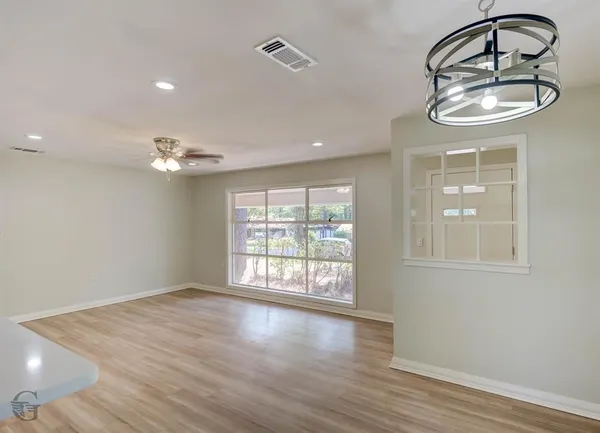 an empty room with wooden floor fan and windows