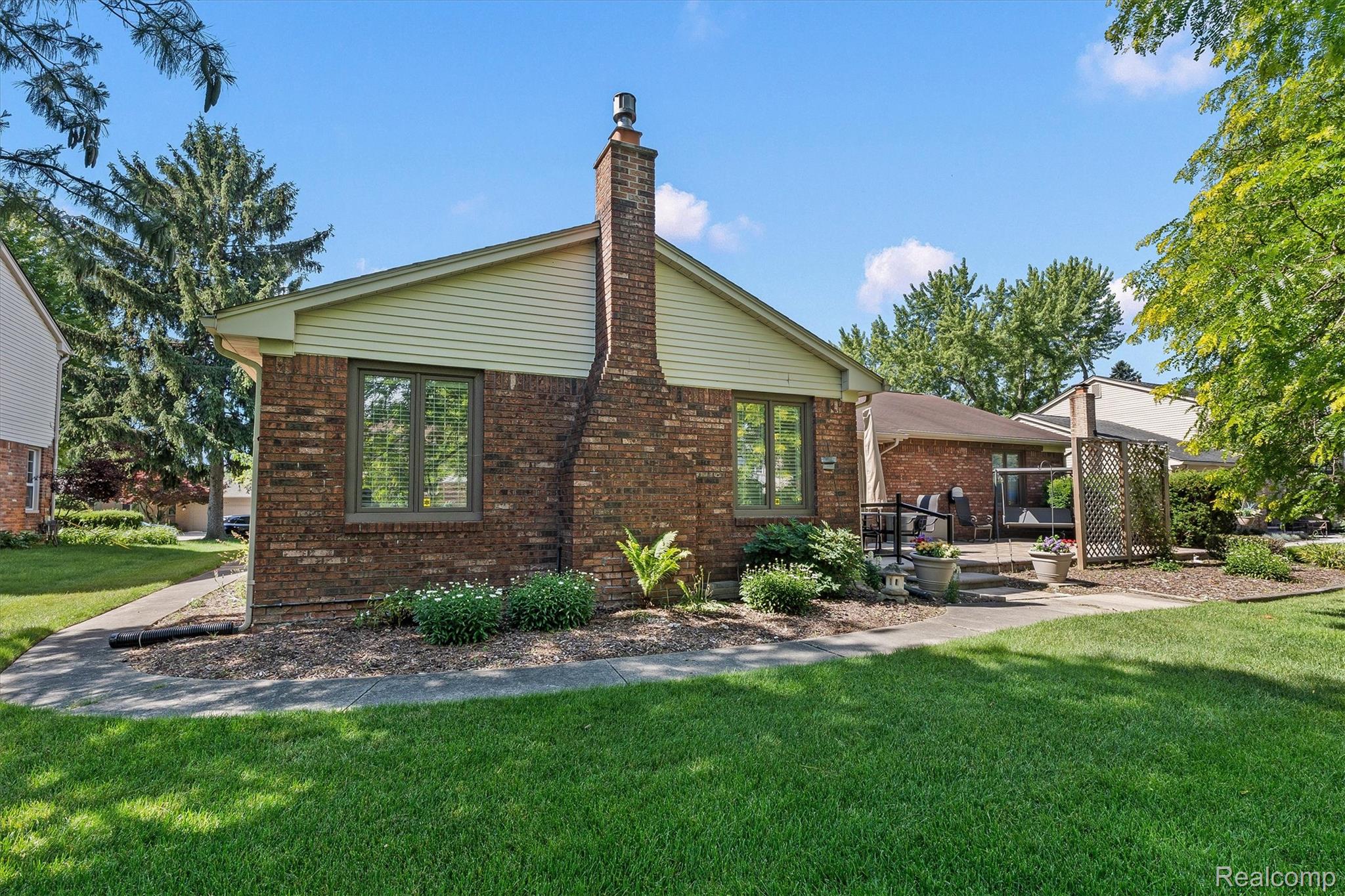 1662 Sumac Drive Rochester, MI 48309 - Photo 32 of 38 Brick exterior featuring a prominent chimney, a rear patio, and a privacy lattice