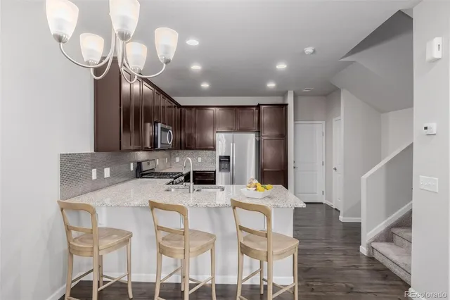 a kitchen with stainless steel appliances kitchen island granite countertop a refrigerator a microwave oven a sink with island and chairs with wooden floor