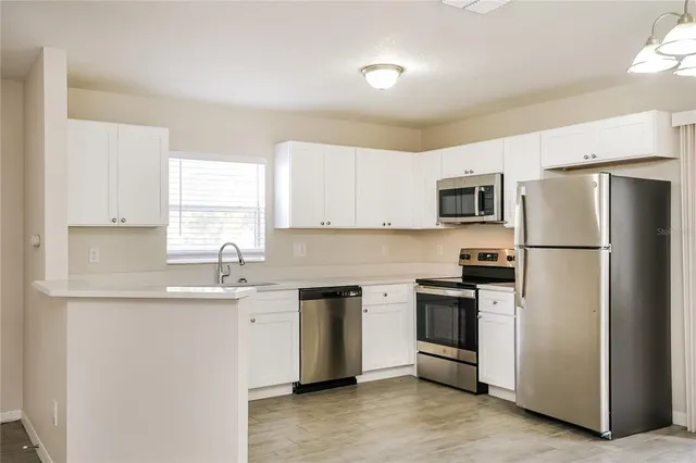 a kitchen with stainless steel appliances granite countertop a refrigerator a sink a stove a microwave and white cabinets