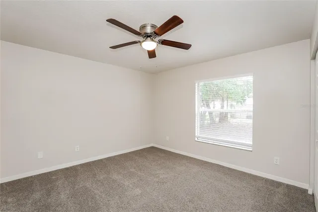 an empty room with ceiling fan and windows