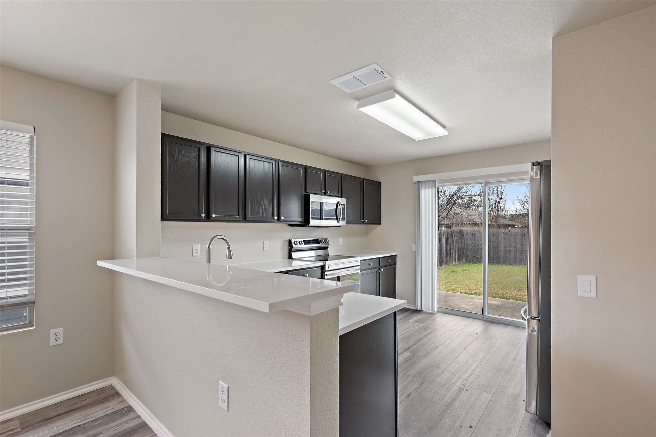1617 Anise Drive Austin, TX 78741 - Photo 8 of 35 Kitchen with light wood-style floors, appliances with stainless steel finishes, light countertops, a peninsula, and dark cabinetry