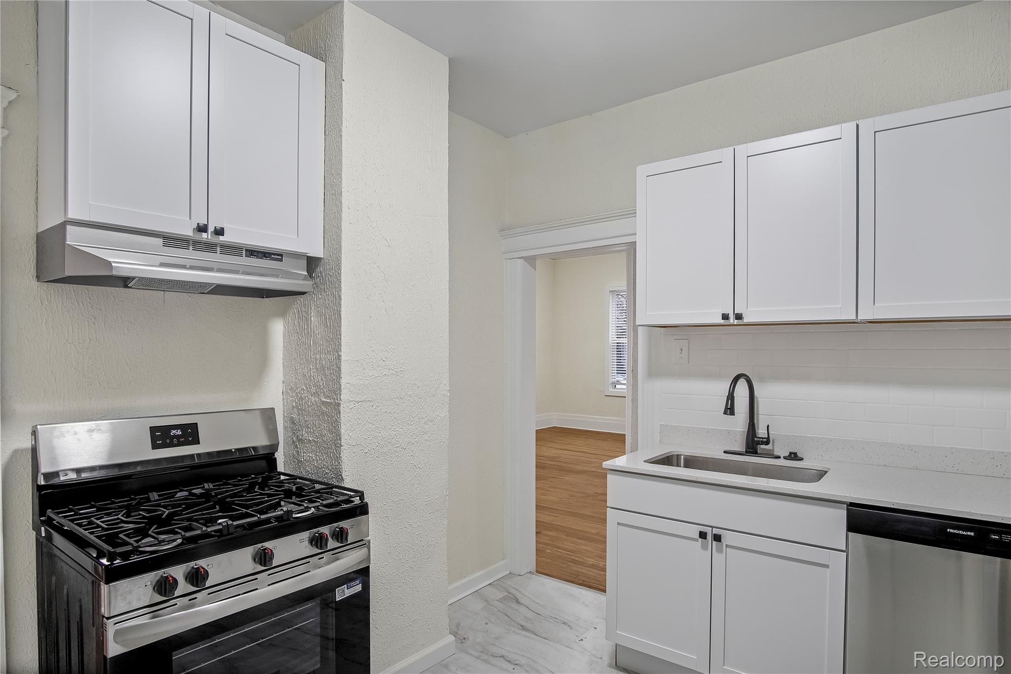 427 Melbourne Street Detroit, MI 48202 - Photo 7 of 29 Kitchen featuring appliances with stainless steel finishes, white cabinetry, under cabinet range hood, light marble finish flooring, and light stone countertops