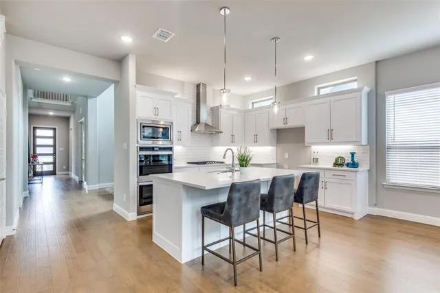 a kitchen with stainless steel appliances granite countertop a kitchen island a stove a refrigerator a sink a dining table and chairs with wooden floor