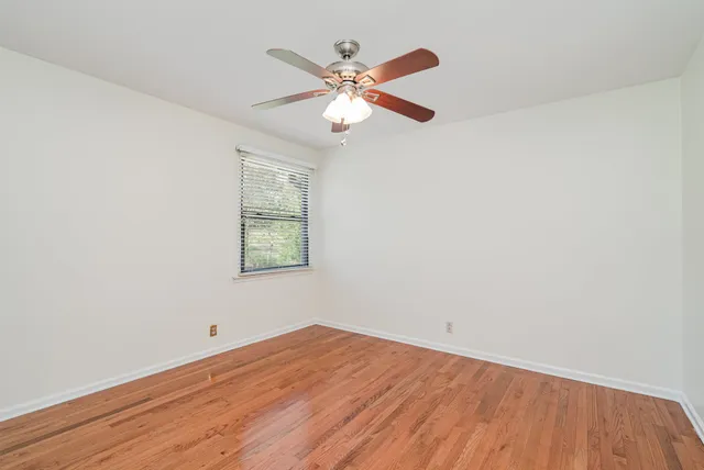 an empty room with wooden floor ceiling fan and windows