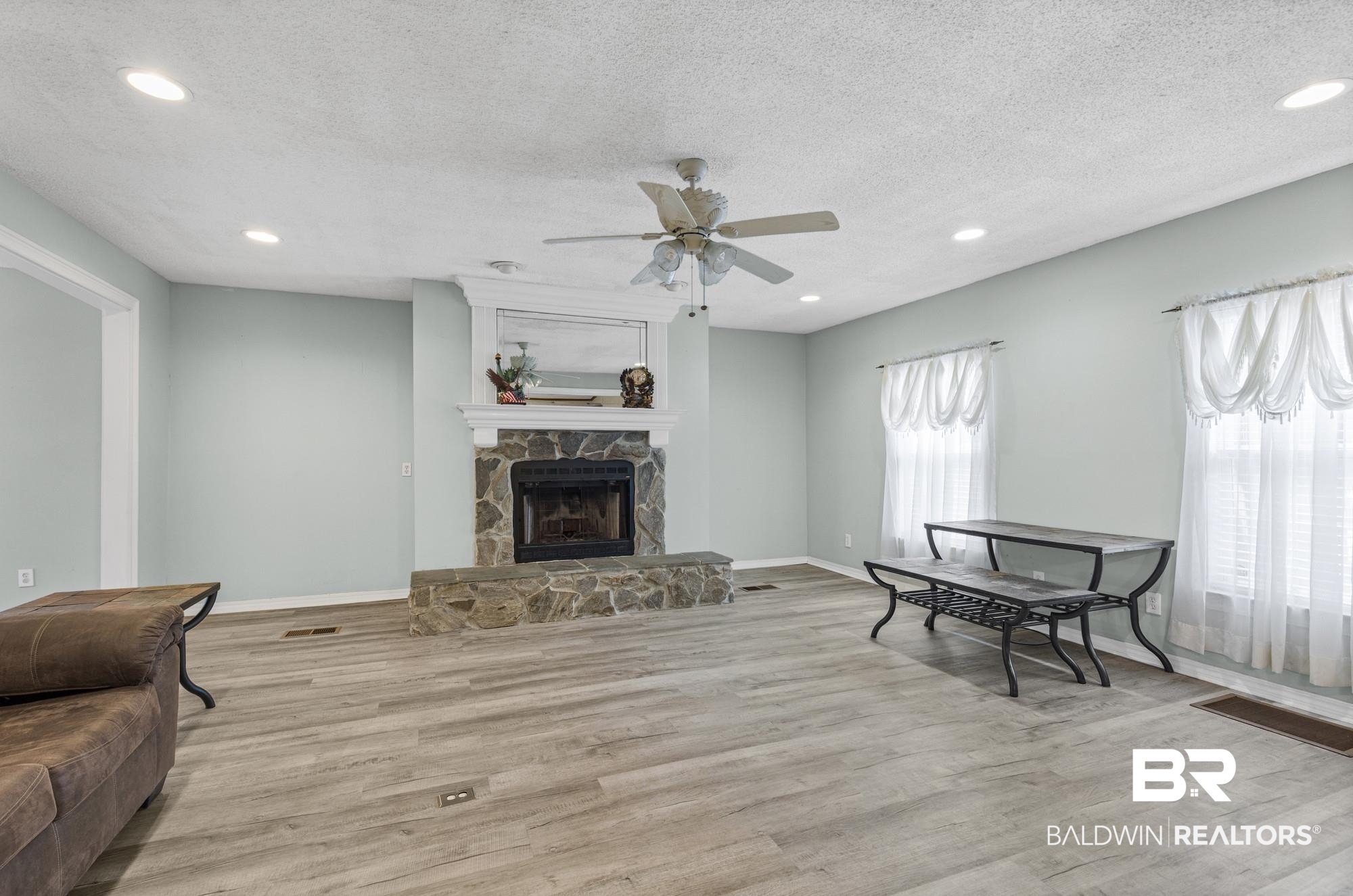 8675 Hunters Pointe Drive North Theodore, AL 36582 - Photo 7 of 20 Spacious interior featuring a stone fireplace with a white mantel, wood-finish flooring, recessed lighting, a ceiling fan, and multiple windows