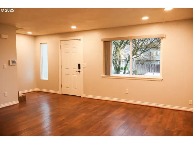 a view of an empty room with wooden floor and a window